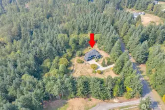 From this soaring drone perspective, the full scope of the property comes into view. The elegant home sits gracefully amidst 5.74 acres of lush, private acreage, with the winding driveway, stone patio, and surrounding landscaping all visible. This vantage point captures the home’s impressive scale, sophisticated design, and serene setting within the gated community, highlighting both its beauty and the expansive natural surroundings.