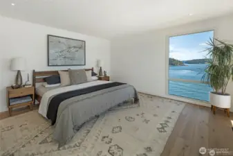 A serene primary bedroom features wide-plank oak floors and soft natural light, framed by a stunning picture window that overlooks the sparkling waters of Cayou Channel. Clean modern lines and warm tones create a calming retreat designed for rest and connection with the island landscape.