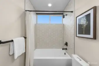 This shower is a statement piece, with crisp hex tilework, matte black accents, and a bright window bringing in natural light.