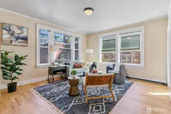Spacious living room with oversized windows, natural light, and refinished original hardwood floors.