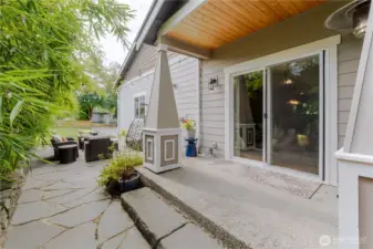 Step outside the living room to a serene patio retreat that is framed by lush greenery, cozy seating, and architectural charm.