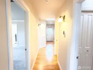 Hallway from great room: L to R; doorway to the Primary bedroom, with ensuite full bathroom, conveniently located closest to the great room.  Further down hallway, L to R is an art niche, the back door, hallway to the other 2 bedrooms, full bath, additional closets, doorway to the 1/2 bath and closest doorway on the right leads to the utility room and garage.