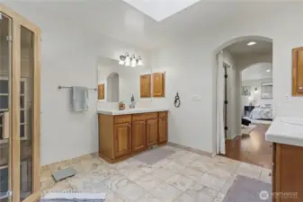 Primary ensuite bath view towards bedroom, his and her closets in the hall. Separate double vanities is a real convenience and I love the tile flooring and skylight!