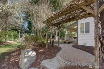 Left-hand side yard view, trellis with grapes! I love the large stone, pavers and all of the landscaping in this large, fully-fenced yard.