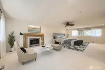A different perspective of the spacious Primary Suite with a sitting area in front of an attractive fireplace, brand new carpet, ceiling fan and a great deal of natural light.