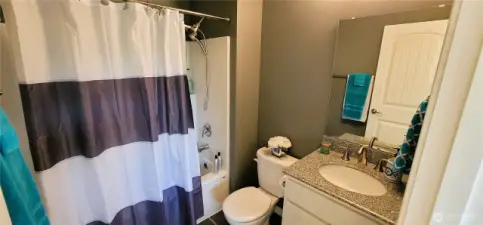 Stylish and serene, the primary ensuite bath offers a clean, modern aesthetic with a granite-topped vanity, striped shower curtain, and sleek fixtures throughout. Thoughtfully designed for comfort and functionality, it’s the perfect complement to this home’s relaxed Surfside elegance.