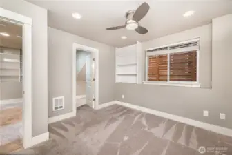 Welcome to the downstairs primary bedroom, complete with built-in shelving, a ceiling fan, spacious walk-in closet, and a private en-suite bathroom.