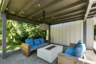 Covered patio featuring cozy seating, a modern fire pit, and whimsical lighting perfect for entertaining!