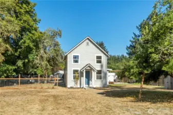 A welcoming stone pathway leads to the front entrance, framed by colorful plantings that add charm and character. The fully fenced side yard on the left provides extra space for gardening, pets, or play..
