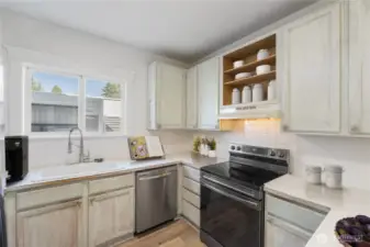 This bright corner of the kitchen features a large window above the sink, stainless-steel / Black appliances, and vintage-style cabinetry. The efficient layout offers plenty of counter space, blending practicality with timeless character.