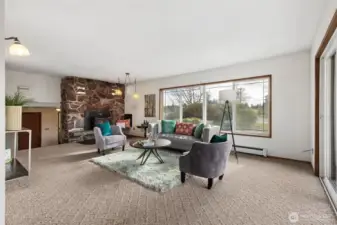 This is another view of the living room showing rock fireplace wall. Look closely at the rock wall toward the top, there are two sets of lights!  With the split level and featured rock wall, it's truly a nod to the mid-century modern era! Baseboard heaters with circulated water throughout home fueled by an oil furnace. NOTE: The baseboard is NOT an electric heater, so it's okay to place furniture there. To the left of fireplace are the steps that lead down to the main entry. The living room is open to the dining room.