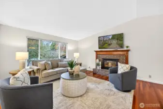 The living room is bright and welcoming, with rich hardwood floors and a classic brick fireplace that anchors the space with warmth and charm. A large picture window brings in beautiful natural light and a leafy outlook, making the room feel calm and comfortable. It’s easy to imagine cozy evenings by the fire or relaxed weekends with plenty of room to spread out.