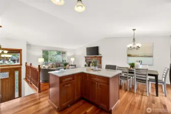 This is the kind of open main level that makes everyday living feel easy, hardwood floors, vaulted ceiling lines, and sightlines that keep everyone connected. The large island with a solid surface counter becomes the natural hub for prep, serving, and casual meals while staying close to the dining area and fireplace. It’s an inviting layout for hosting, relaxing, and simply enjoying the flow of the home.