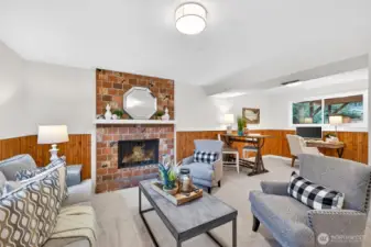 This angle shows just how versatile the lower level is, offering plenty of room to spread out with a comfortable lounge area anchored by the brick fireplace and crisp white mantle. The wood wainscoting wraps the space in a classic, Northwest feel, and the open layout easily supports multiple zones. You can entertain, relax, and still have space for hobbies or a work area, all in one welcoming room.