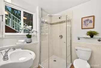 This bathroom feels bright and polished, featuring a glass enclosed shower with classic white tile and a decorative accent band for a tailored finish. The pedestal sink, chrome fixtures, and beadboard wainscoting deliver that timeless look buyers love, and the window adds natural light and ventilation. It is a space that feels fresh, functional, and ready from day one.