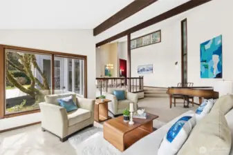 This perspective really captures the soul of the space. That moss-covered tree just outside the window becomes its own focal point, almost like a living sculpture that’s been quietly growing into place for decades. It adds a sense of calm and history you can’t replicate. Inside, the scale of the room stands out, easily accommodating a baby grand piano, and with those vaulted ceilings, you can imagine the acoustics are just as impressive as the view. The subtle step down from the dining area creates that classic sunken living room feel, but here it reads more refined than retro. From this angle, you can also see the connection back to the dining room and toward the entry, keeping everything visually open while still giving each space its own identity.