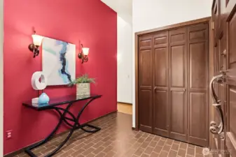 A warm, inviting first impression with just the right amount of character. The brick-style paver tile underfoot sets a grounded tone, while the accent wall in a rich terracotta hue adds depth and warmth without overpowering the space. It’s a natural landing zone when you walk in, with a large coat closet tucked behind wood bifold doors to keep things organized. The front door is a standout, solid wood with a beautifully detailed, scrolled handle that feels like a nod to the home’s original era in the best way. Vaulted overhead, the space feels open and airy, but still anchored with that vintage charm that gives it personality.