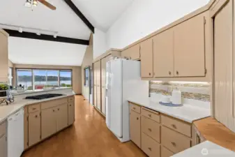 Cooking here doesn’t feel tucked away, it feels like part of the experience. The gas cooktop sits right across from the breakfast bar, so conversations flow easily while meals come together. Look past it and you’ve got that wide water view framed through the family room, which adds a whole different level to the space. The kitchen itself leans bright and clean with white appliances, including a French door fridge with built-in water and ice, and light granite countertops that keep everything feeling open. The backsplash mixes white and warm tones in a way that ties in with the cabinetry without being too matchy. And although you don’t see it here, there’s a wall oven with a microwave above just off to the side, giving you extra cooking capacity when you need it. It’s a layout that feels social, functional, and just easy to be in.