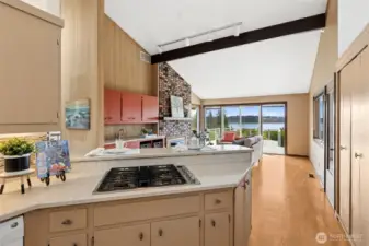 This angle shows how naturally everything comes together. Cooking at the gas range, you’ve got a clear line of sight across the breakfast bar, through the family room, and out to the water, which keeps the whole space feeling open and connected. The pantry sits nearby for easy access, and just next to it, the exterior door leads straight out to the covered porch, making outdoor entertaining feel effortless instead of complicated. The color palette stays warm and inviting, tying the kitchen and living spaces together.