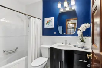 A great mix of function in the main bathroom. The solar tube brings in natural light from above, keeping the room feeling open and bright without needing to rely on overhead lights all day. The tub and shower combo is ready for everyday use, and the tile surfaces keep things low maintenance. There’s plenty of storage built into the vanity with extra drawers, and the beveled mirror adds a nice finishing touch. The blue accents bring energy to the space, balanced by the white granite counters for a clean, polished look.