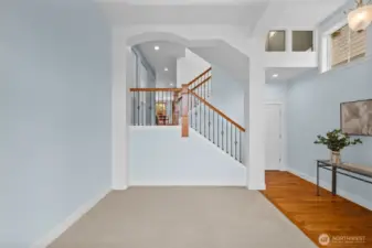 The living room opens to the main-level staircase, with high windows creating a sun-filled, welcoming ambiance.