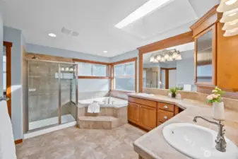 Stunning, luxurious en-suite primary bathroom filled with natural light from a skylight and abundant windows and storage. There is a convenient linen closet tucked to the left.