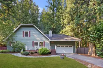 This charming home instantly feels inviting with its classic front porch, cheerful shutters, and lush landscaping. Nestled among tall evergreens, it exudes a cozy, homey feel that’s both welcoming and serene.