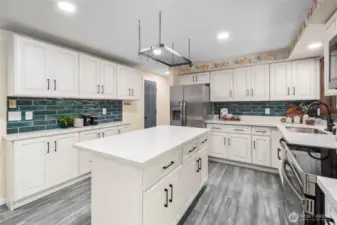 An abundance of cabinetry provides exceptional storage in this bright, uplifting kitchen. Light finishes and recessed ceiling lights enhance the airy feel, beautifully contrasted by the rich green tile backsplash with matching color doors. A charming floral accent along the upper wall adds a touch of personality and warmth.