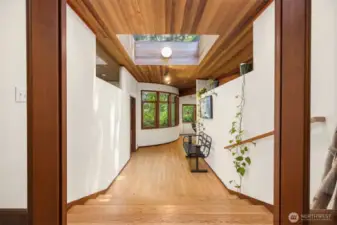 This artful main floor hallway is bathed in natural light from an oversized skylight and curved window wall, creating a bright, inviting path through the home