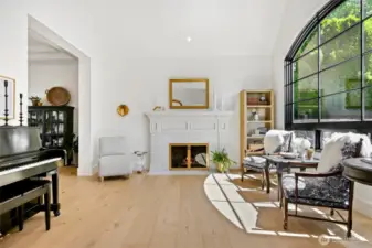 Sophisticated formal living room showcases a marble fireplace, vaulted ceilings, and stunning floor-to-ceiling arched window—perfectly blending classic elegance with modern light-filled design.