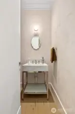 Chic powder room with a sculptural marble sink, elegant wall-mounted mirror, and soft plaster-finish walls—blending modern luxury with timeless style.