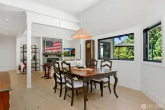 Bright dining area with large picture windows, vaulted ceilings, and wide-plank hardwood floors—seamlessly connected to the living space with a cozy fireplace and custom millwork detailing.