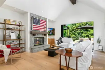 Inviting living room with vaulted ceilings, gas fireplace framed in stone, and seamless indoor-outdoor flow through a 10 foot  bi-folding sliding glass door to a private deck with views of Lake Sammamish.
