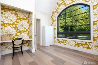 Charming flex space on the main floor bathed in natural light, featuring vaulted ceilings, a bold designer accent wall, and oversized arched window—ideal for a home office, creative studio, or cozy reading nook.