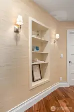 Charming hallway nook with built-in display shelving, grass cloth wall covering, and elegant sconces—adds character and functionality to the transitional space.