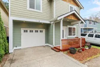 Covered front porch with wood railing creates a welcoming entry. Attached single-car garage and concrete driveway provide convenient off-street parking.