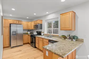 Kitchen with granite countertops, wood cabinetry, and appliances including a new refrigerator and new microwave. Window above the sink provides natural light and backyard views.