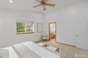 Primary bedroom with high ceiling and ceiling fan, offering ample space for furnishings. Large window provides natural light and views of the surrounding greenery.