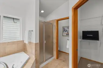 Primary bathroom featuring a soaking tub with tile surround and a separate glass-enclosed shower. Window above the tub brings in natural light.