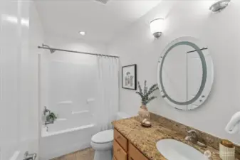 Full bathroom with granite vanity countertop, wood cabinetry, and a tub/shower combination with tile surround. Neutral finishes create a bright and functional space.
