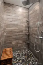 Shower room with large walk-in shower with slate tile, rock flooring, waterfall/stream shower head, and towel warmer.