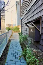 view from shared secured pedestrian walkway (locked gate). mailboxes on right. car entrance seen across the shared driveway