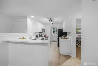 Quartz-capped breakfast bar introduces the renovated kitchen, showcasing crisp white cabinetry, sleek stainless appliances, and durable LVP flooring—an ideal spot for casual dining or conversation while meals are prepared.