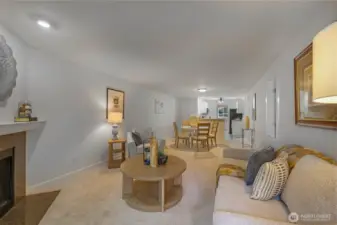 An elongated sightline from fireplace to kitchen emphasizes the open-concept design, fresh interior paint, and new carpet that together create a bright, move-in-ready backdrop.