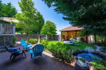 The backyard oasis is a standout, complete with a lush lawn, covered gazebo, water feature, and lounging space—ideal for entertaining or simply enjoying a summer day.
