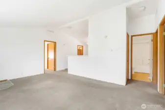 From a corner in the living room, you can see the primary bedroom door to the left, the kitchen half-counter, and the doorways to the other two bedrooms and full main bathroom.