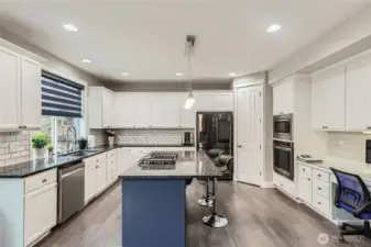 Beautifully updated kitchen showcases white soft-close cabinetry, granite countertops, full-height backsplash, stainless steel appliances, a center island, and planning desk.