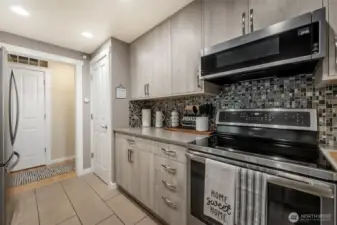Beautifully updated kitchen with custom cabinetry, quartz countertops, sleek backsplash, stainless steel appliances + convection oven, ambient floor lighting, tile flooring, and pantry