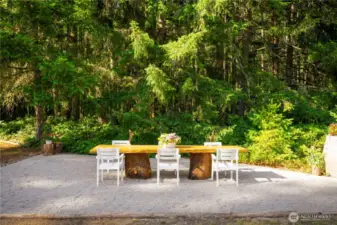 The outdoor dining area is surrounded by trees and the meadow and defined by logs from the property.
