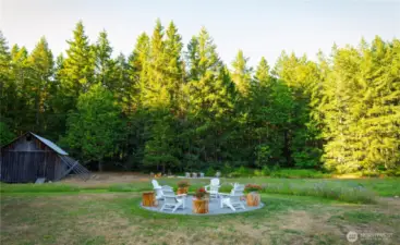 The fire pit space with the historical barn to the left and the dining area beyond, among the wildflower meadow.